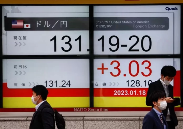 Passersby walk past electric monitors displaying the exchange rate between the Japanese yen against the U.S. dollar outside a brokerage in Tokyo, Japan January 18, 2023. REUTERS/Issei Kato